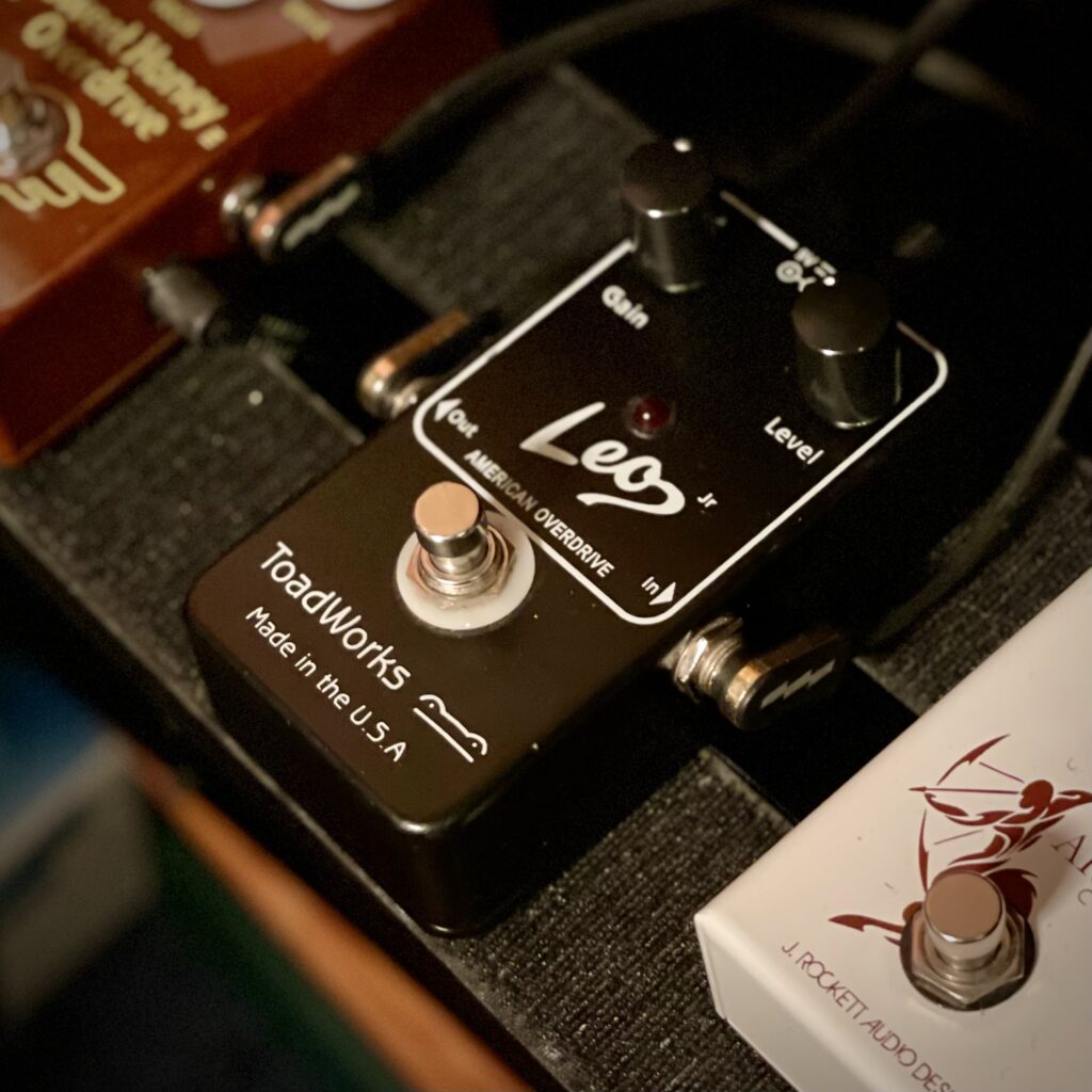 The photo shows the ToadWorks Leo Jr pedal, photographed from an angle above.

The pedal itself is black, with a gain knob at the top left, and a level (volume) knob at the top right.