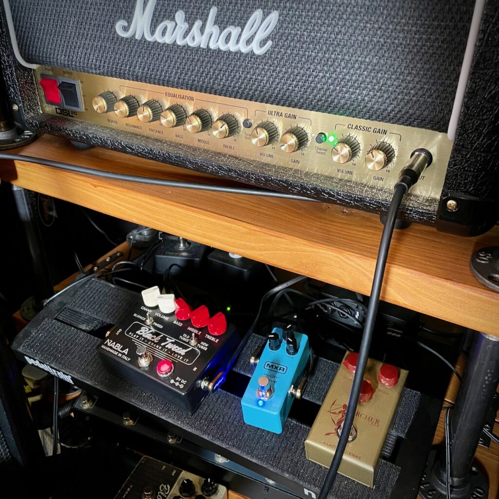 This photo shows my Marshall DSL20HR amp head on a shelf, and my pedal board on a second shelf below.

The Marshall DSL20HR is on the clean channel, and the controls can be seen as follows:

* reverb: off
* resonance: about 8 o'clock
* presence: about 12 noon
* bass: just below 10 o'clock
* mids: about 10:30
* treble: about 1:30
* volume: about 10 o'clock
* gain: about 11 o'clock

On the pedal board, we can see three pedals: the NABLA Custom Black Tweed, the MXR Sugar Drive, and the JRAD Archer Ikon.