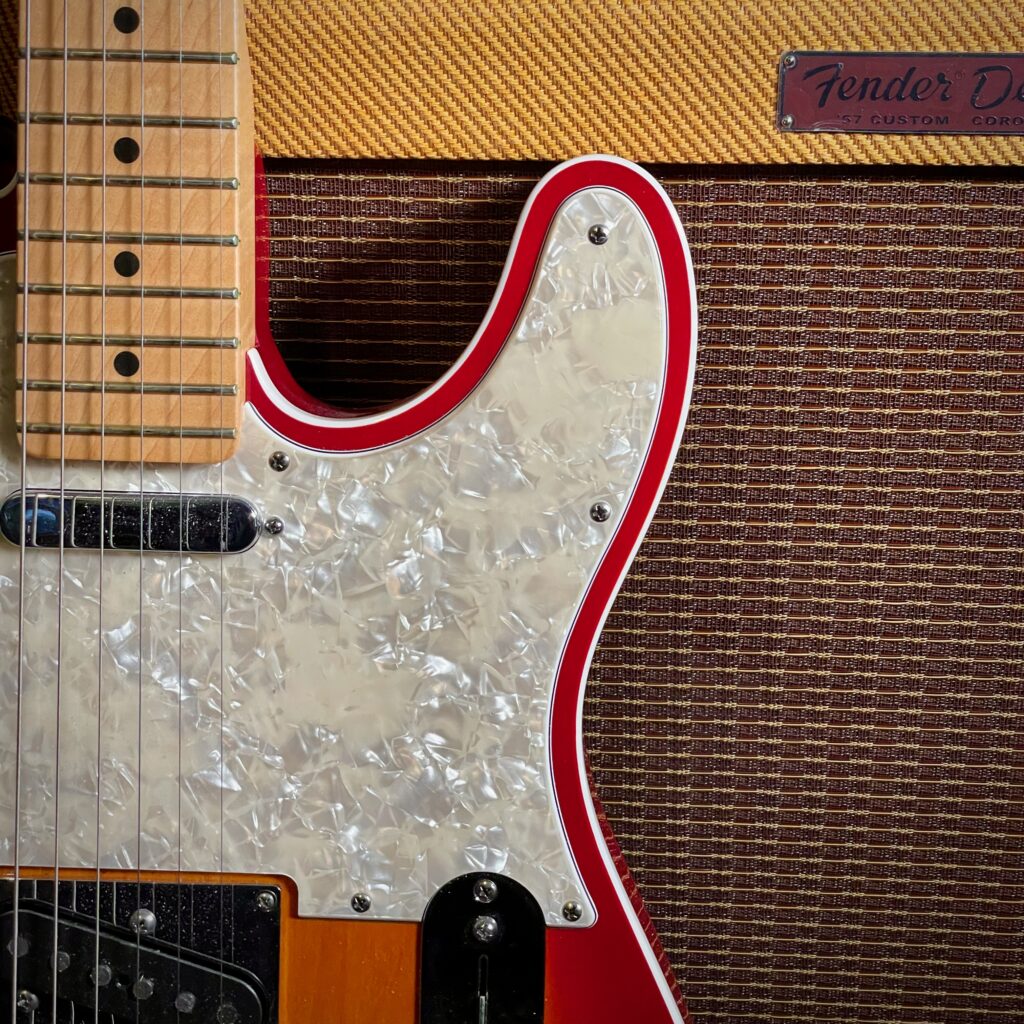 This photo shows a close-up of a Telecaster leaning against the front of a Fender Tweed Deluxe amplifier.

The photo is framed to show both Telecaster pickups, most of the pickguard, and the beginnings of the Telecaster's control plate.