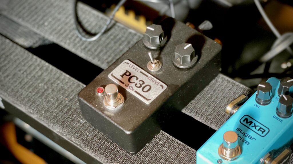 The photo shows a rather dusty-looking pedal in a black enclosure.

There are two control knobs, labelled Level and Drive. Also shown is a toggle switch, which is (if you zoom in a lot) has settings labelled 'D' and 'S'.