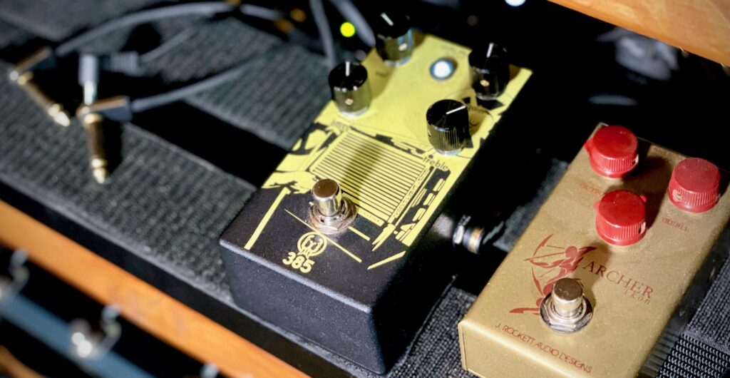 This photo shows the Walrus Audio 385 Overdrive pedal on my pedal board.

It has a black enclosure, with yellow print on the top. The yellow print depicts an old cinema projector.

There are four block control knobs shown.

Next to the 385 is my Archer Ikon pedal. Side by side, the 385 looks a good 25% larger in all dimensions: width, height and depth.