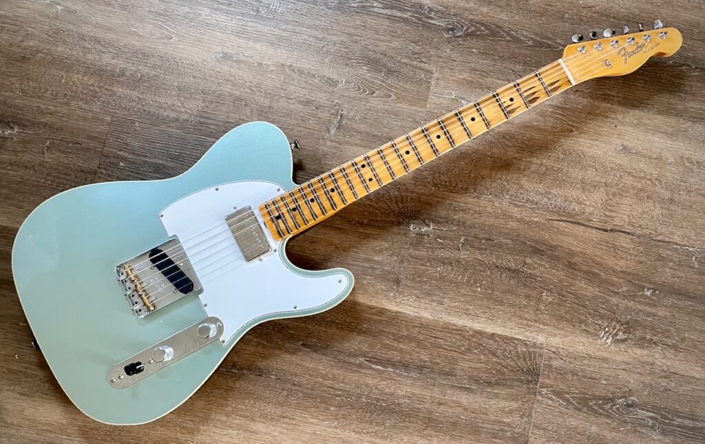 This photo shows a top-down view of my new Telecaster, laid on its back on a wooden floor.

The heavy relicing of the all-maple neck really stands out, along with the silver-green body, and the all-back bridge pickup.