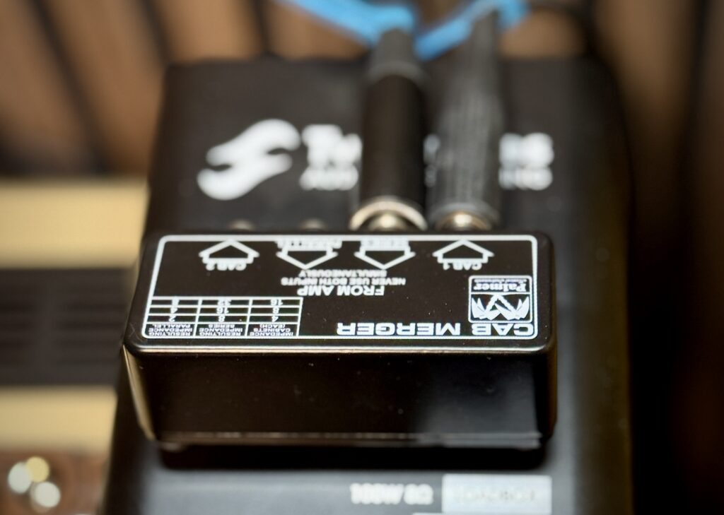 This is a photo of the Palmer PCABM.
The top of the PCABM is visible, but facing away from us (so that the cables plugged into the PCABM are facing the back of my amplifier).
There are two cables plugged into the PCABM: one in the "Series In" input (from my amplifier), and one in the "Cab 1" output (to the Two Notes Captor).
At the very top of the photo, there is a blue tag around each cable. Yes, dear regular reader, I finally started labelling my cables! Why didn't I do this sooner?!?